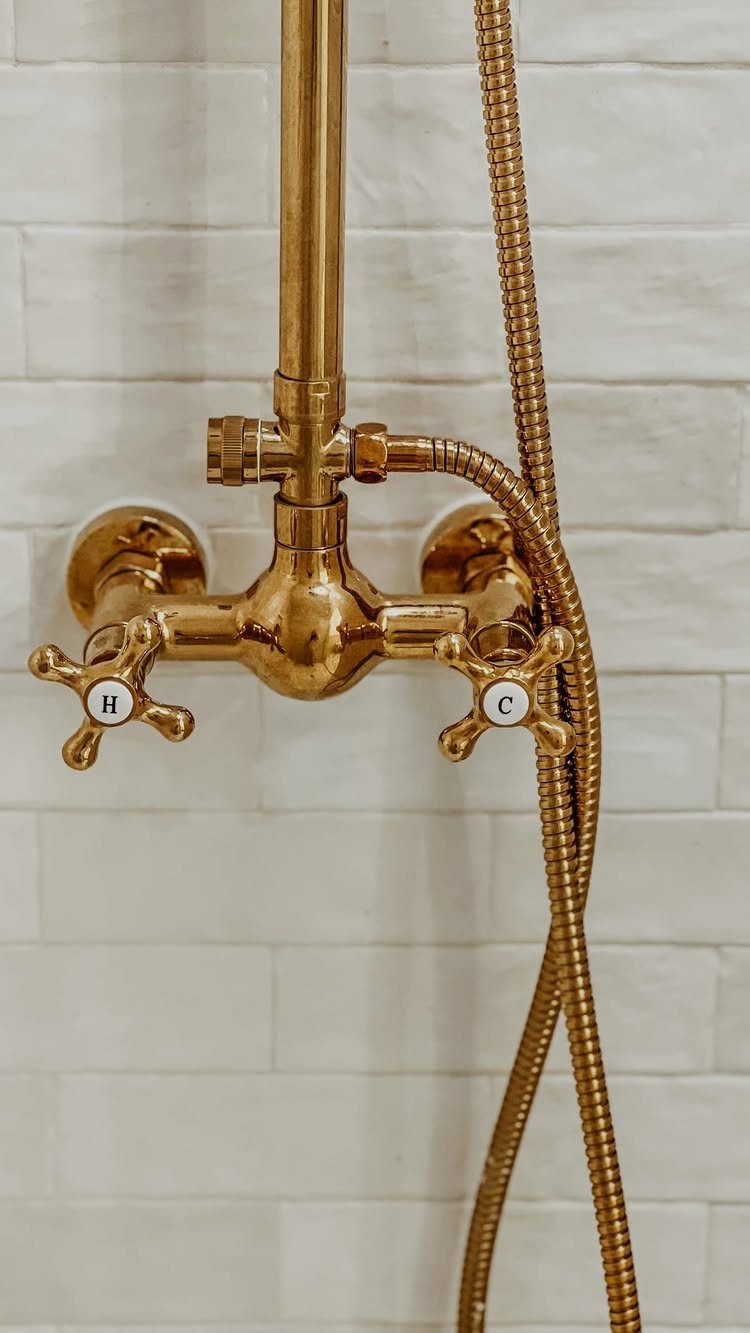 Gold brass shower faucet with cross handles mounted on a white subway tile wall.