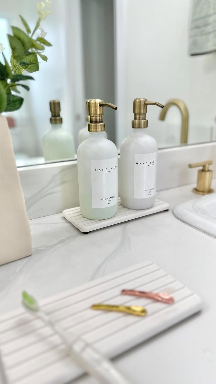 Two white glass soap dispensers with gold pumps resting on a marble tray.