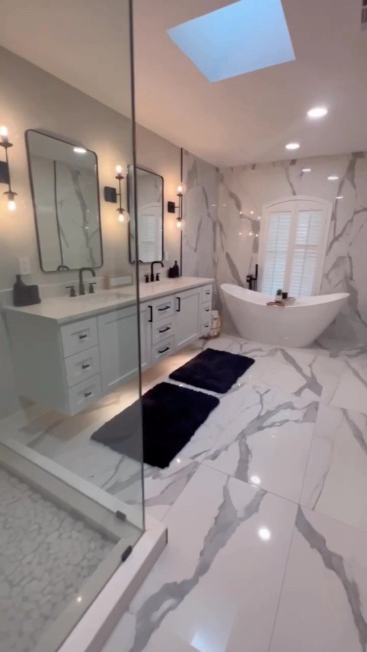 A luxurious bathroom with marble flooring, a long white vanity, and a large freestanding soaking tub.