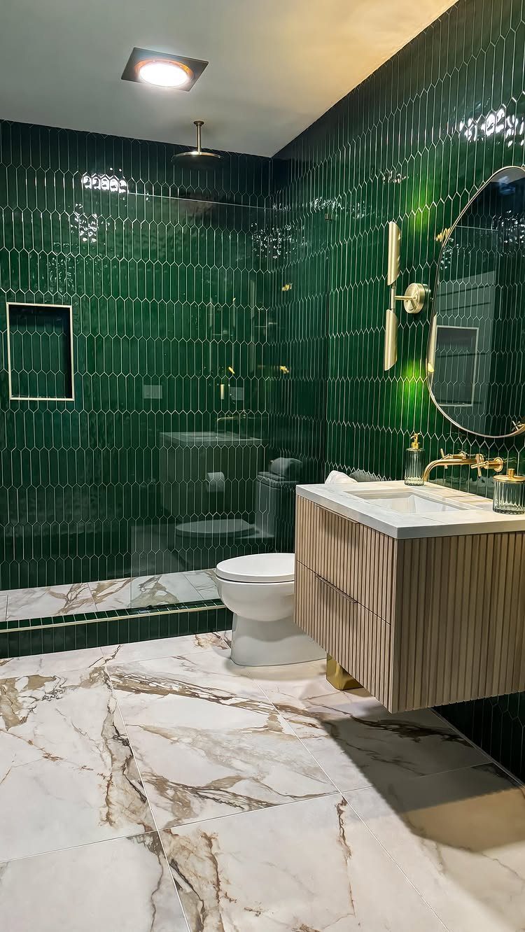 Emerald green vertical subway tiles cover the walls of a modern bathroom with marble floors.
