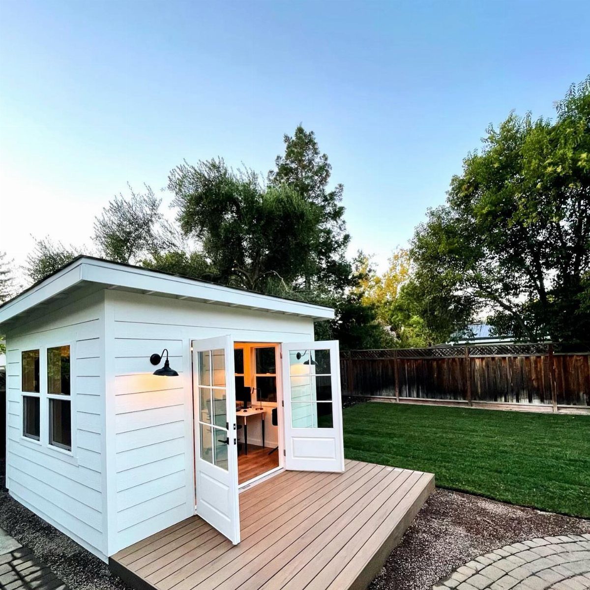 White wooden garden shed with an open door revealing a small home office interior.