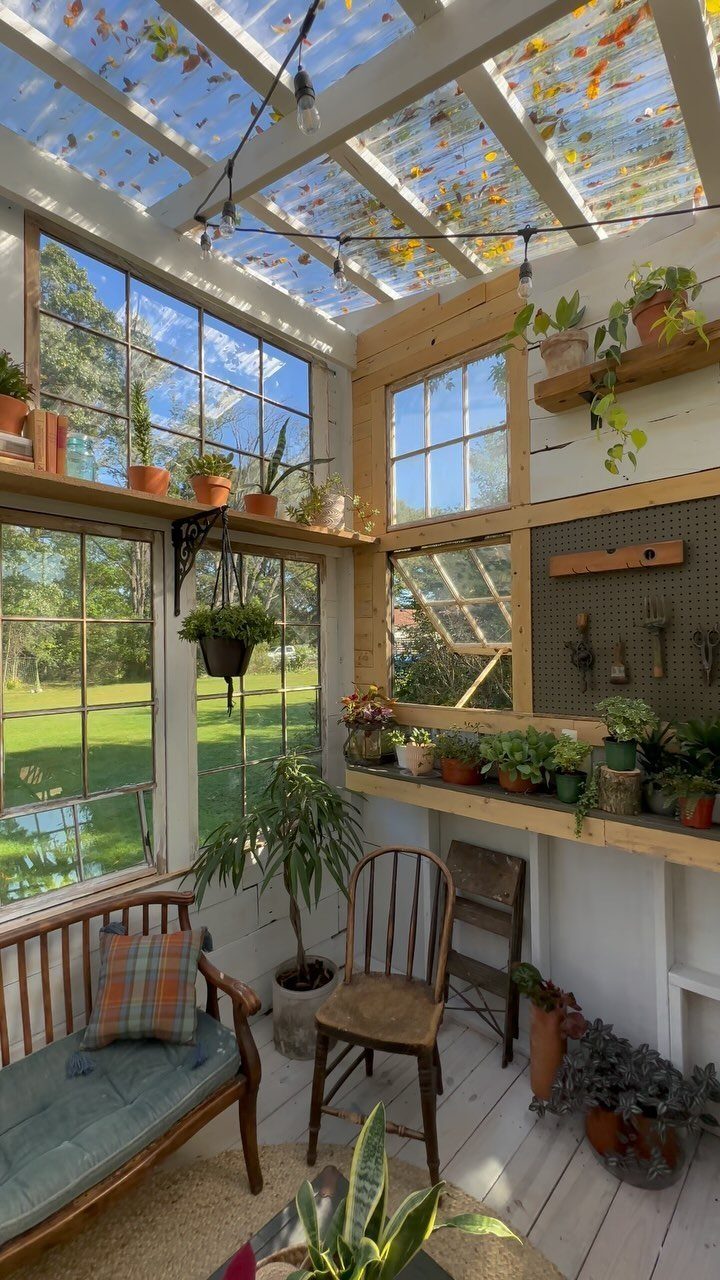 Interior of a bright garden studio filled with many potted plants and wooden furniture.