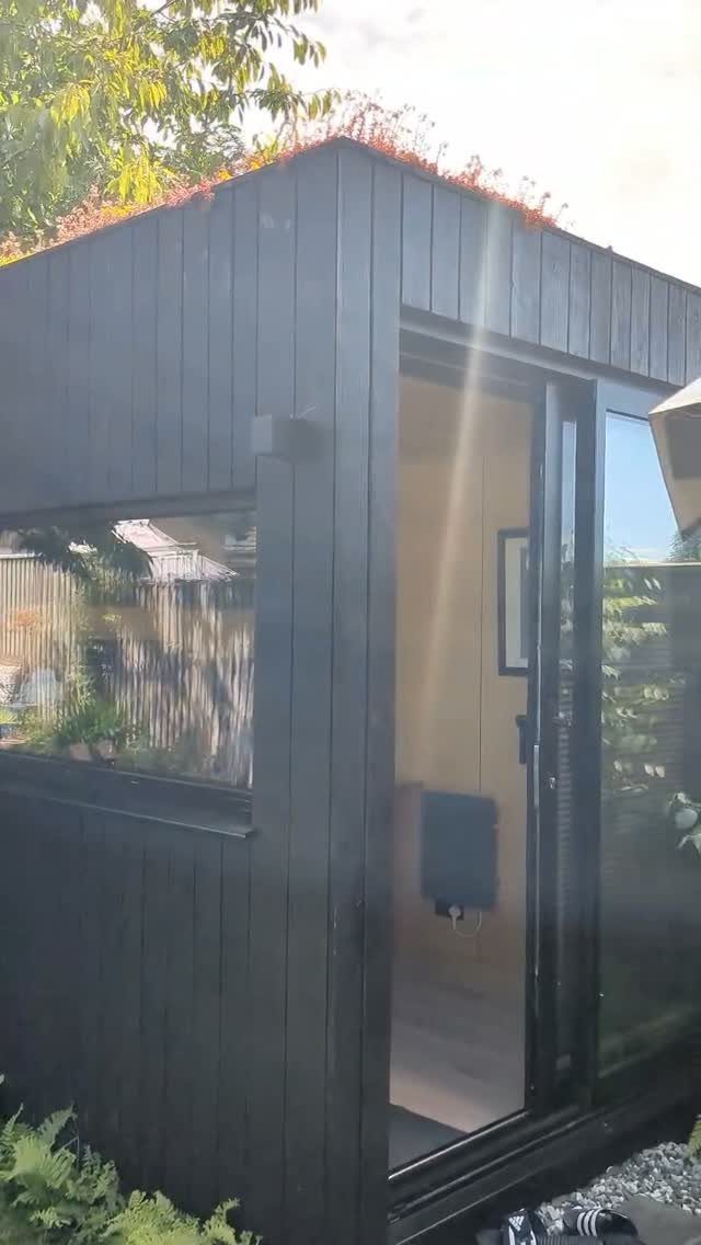 Black wooden garden studio with large glass doors and a side window in a garden.