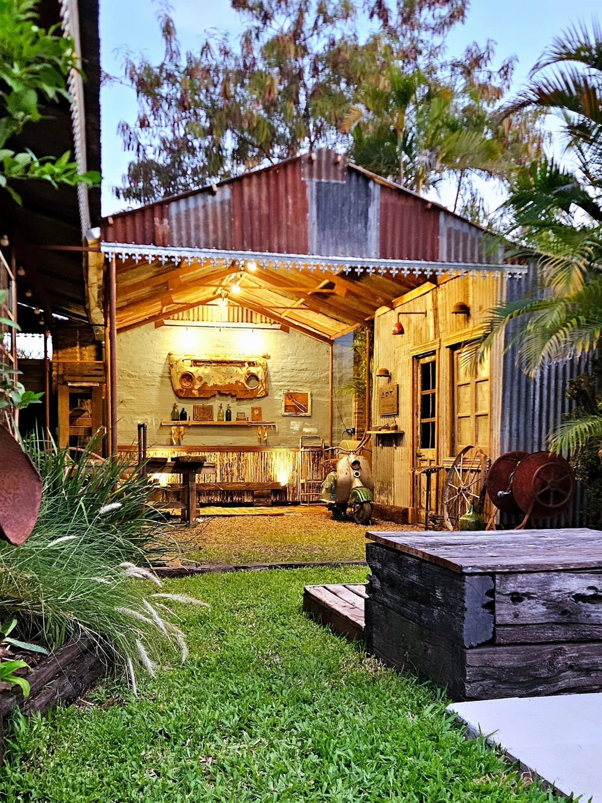 A rustic garden shed constructed from corrugated metal and weathered wood panels surrounded by greenery.