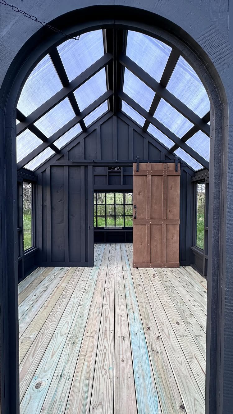 Black wooden shed interior featuring a natural wood barn door and a translucent skylight roof.