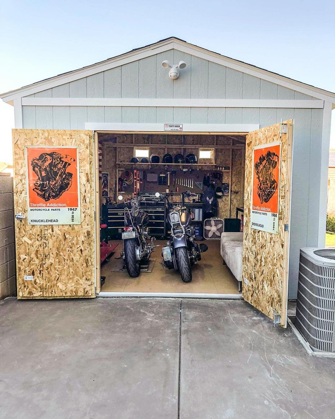 Two motorcycles parked inside an open wooden shed filled with tools and equipment.