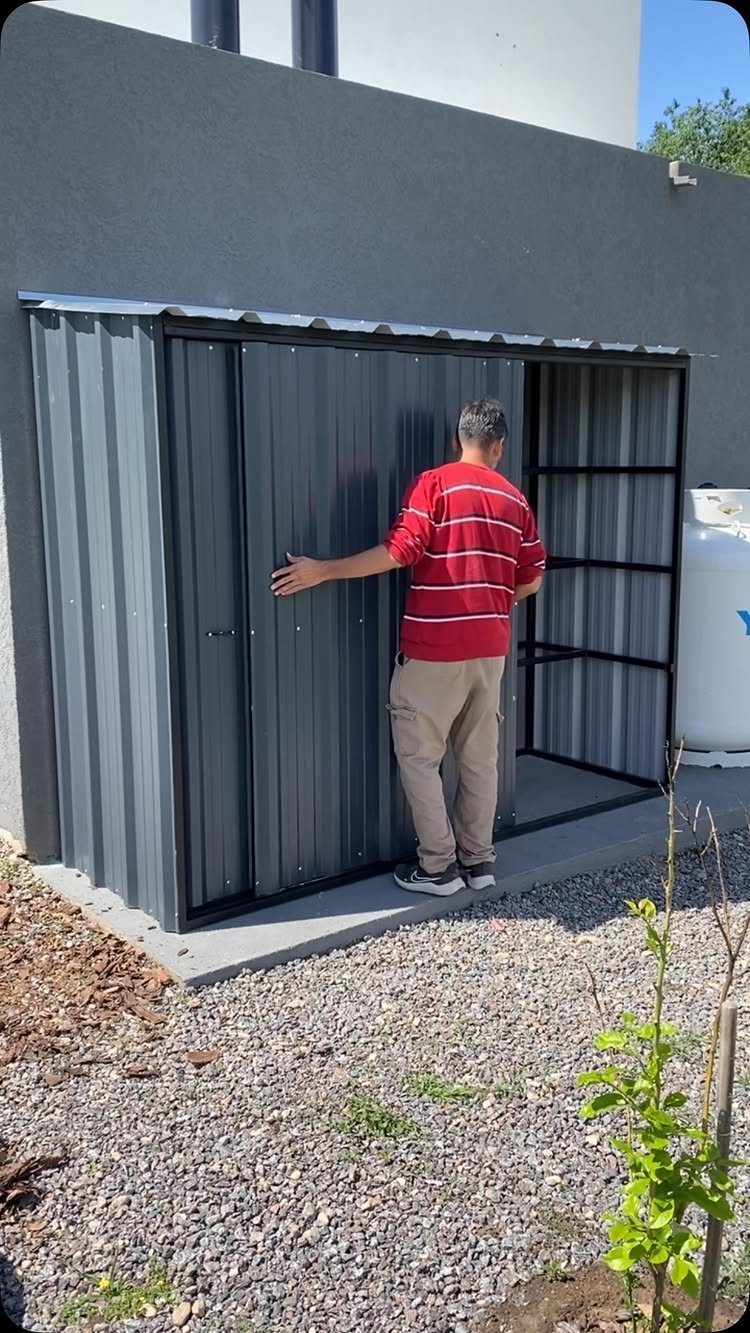 A man stands in front of an open dark grey corrugated metal storage shed.