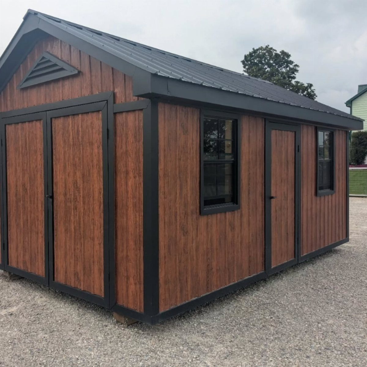 A wooden shed with black trim and a dark metal roof sitting on gravel.