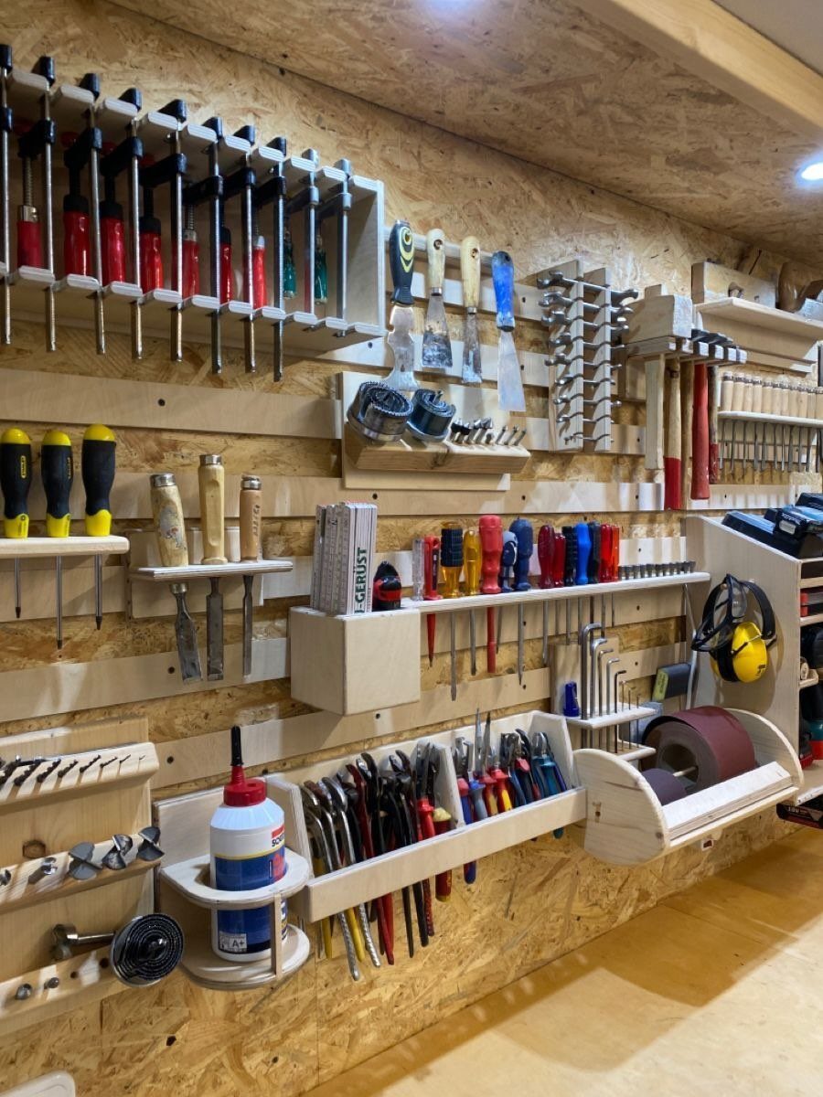 Various hand tools organized in wooden holders mounted on an oriented strand board workshop wall.