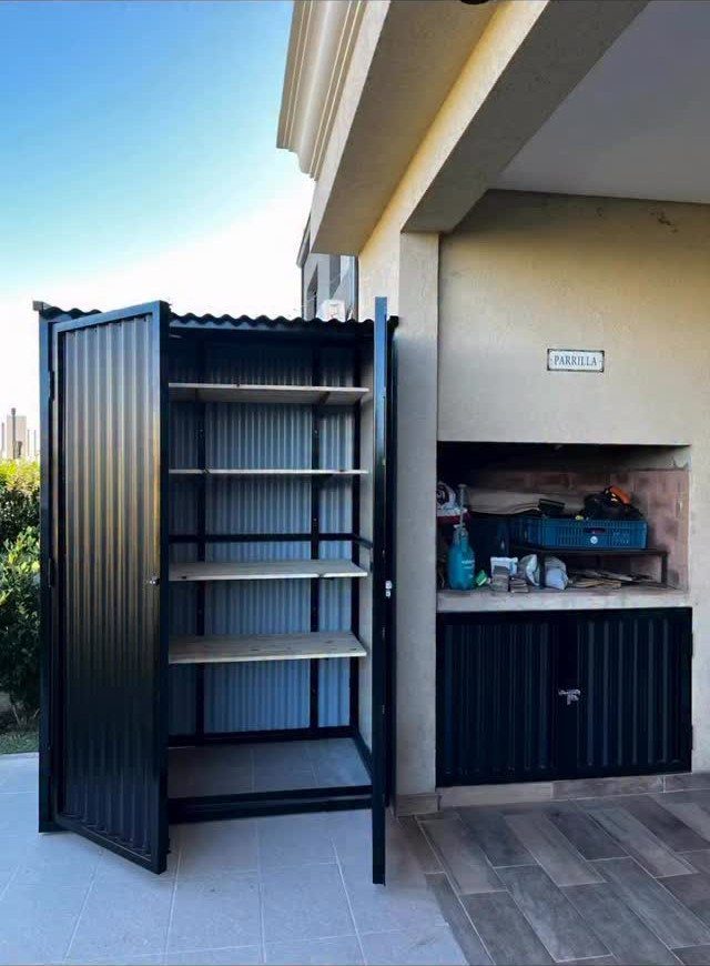 Open black metal storage shed showing four wooden shelves inside on a tiled patio.