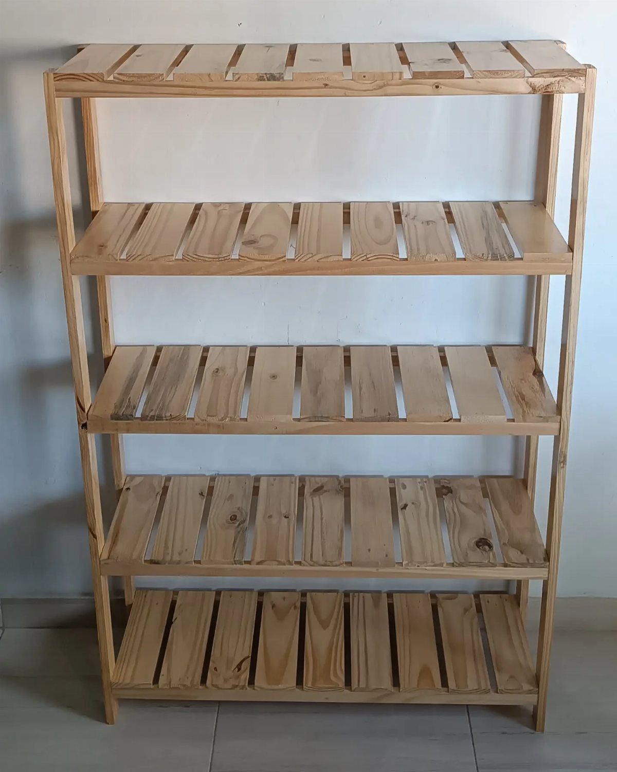 A five-tier wooden shelving unit made of light-colored slats against a white wall.
