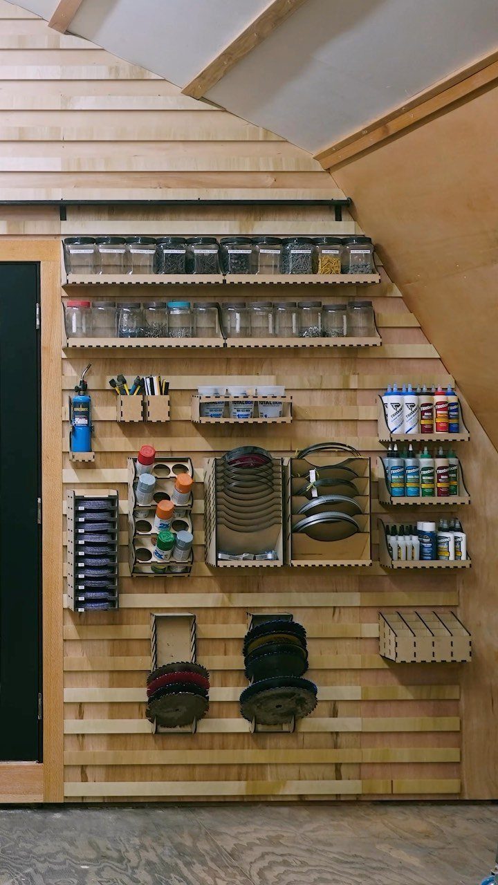 Wooden wall with a French cleat system holding various storage bins and tool organizers.