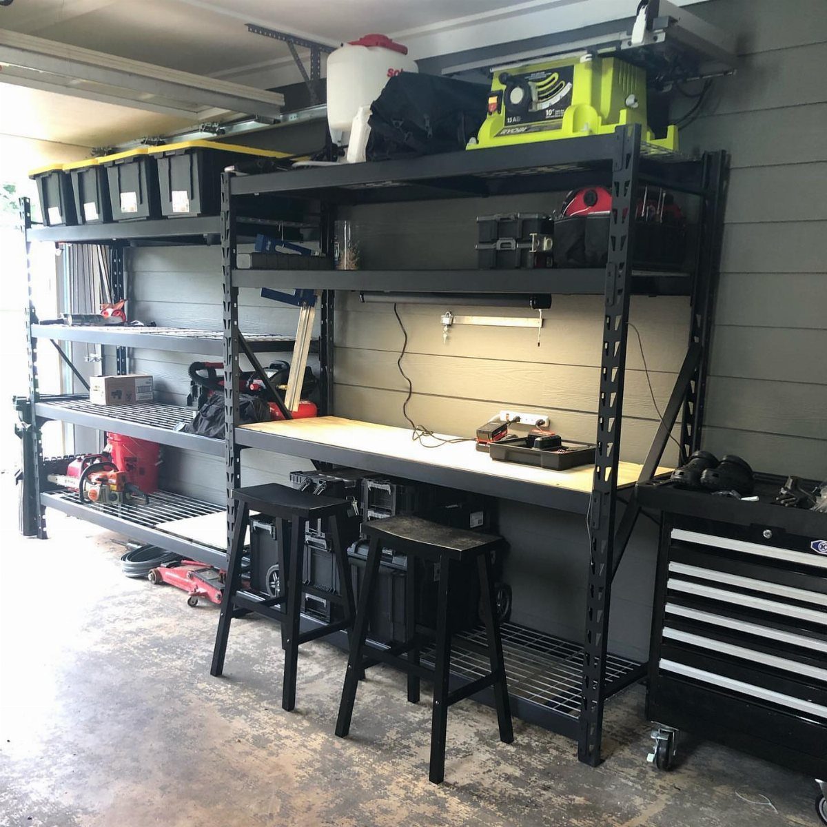 Black metal garage shelving units with a wooden worktop and storage bins in a garage.