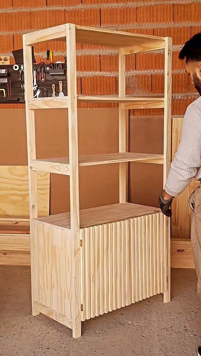 A tall handmade wooden shelving unit with three open shelves and a slatted cabinet base.