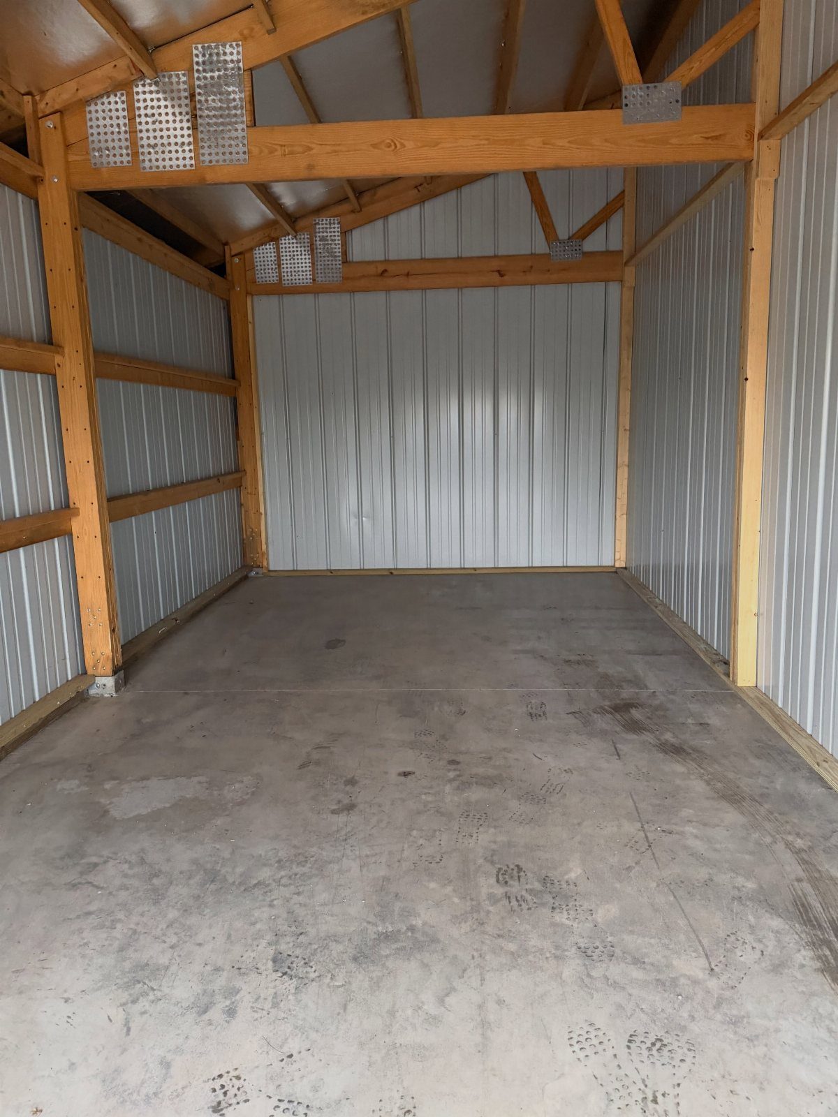 An empty wooden shed with metal walls and a bare concrete floor.