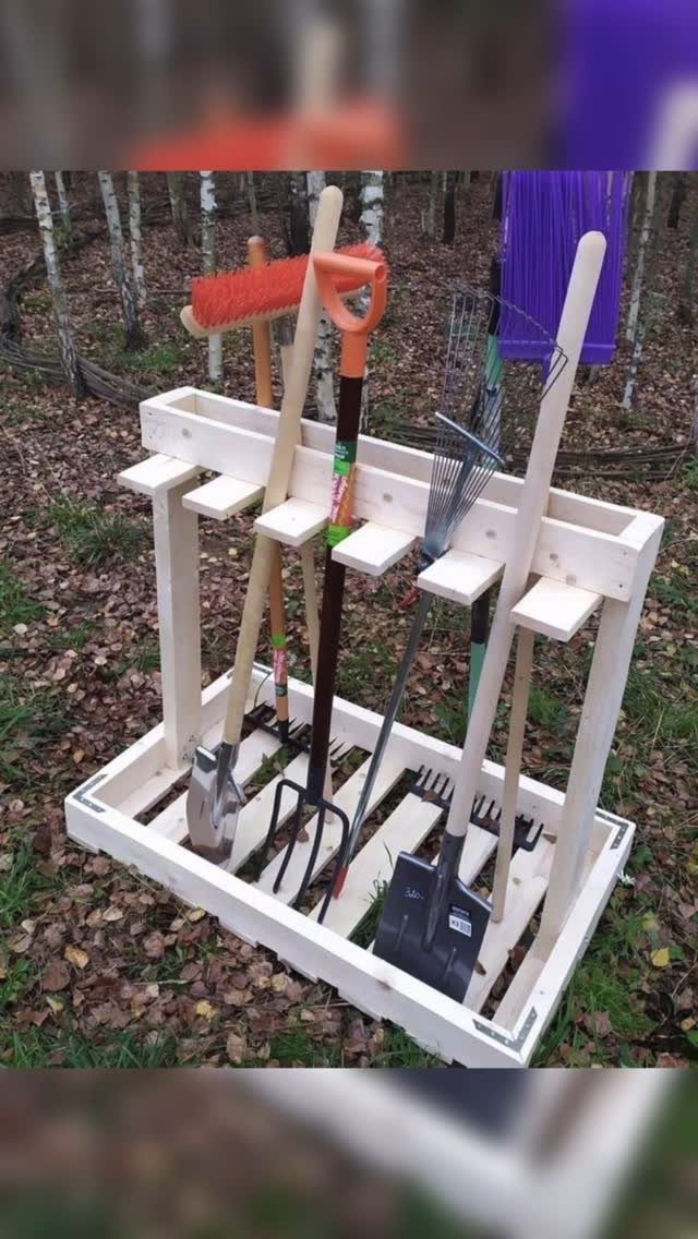 Wooden garden tool organizer holding various shovels and rakes on a bed of autumn leaves.