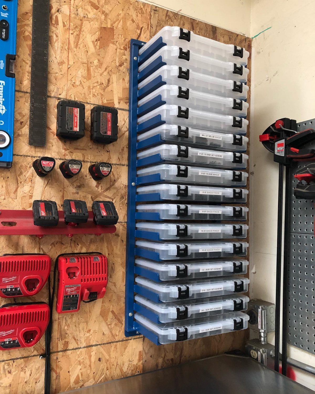 Organized workshop tools and clear plastic storage bins hanging on an OSB wood wall.