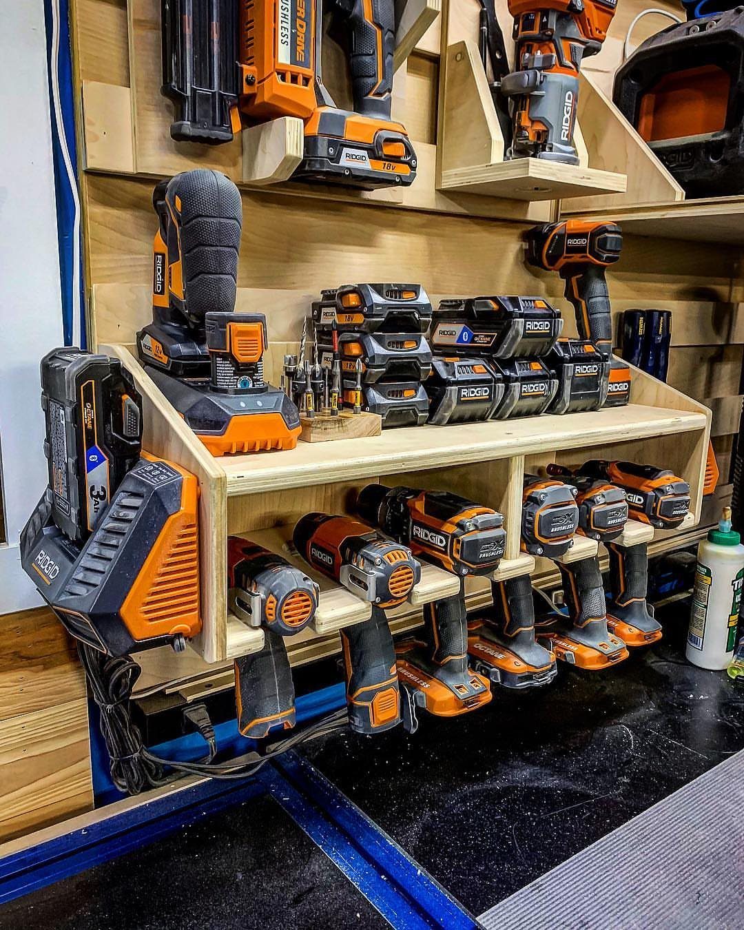 Orange and black power tools organized on a custom wooden shelving and rack system in a workshop.