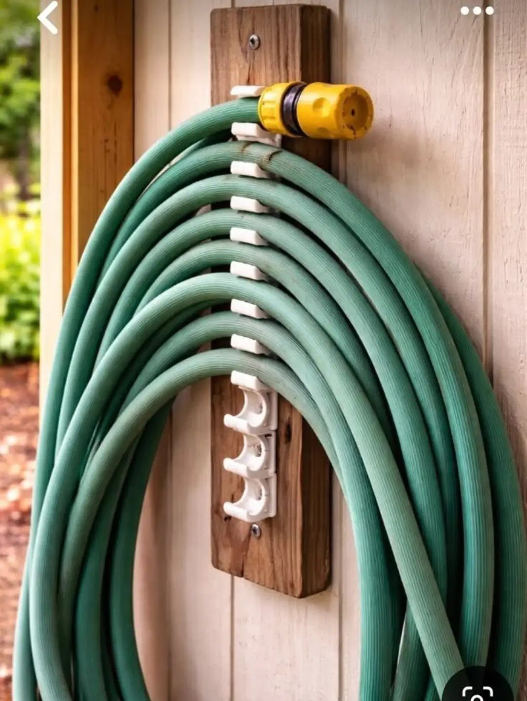A green garden hose coiled neatly on a white plastic wall-mounted storage rack.