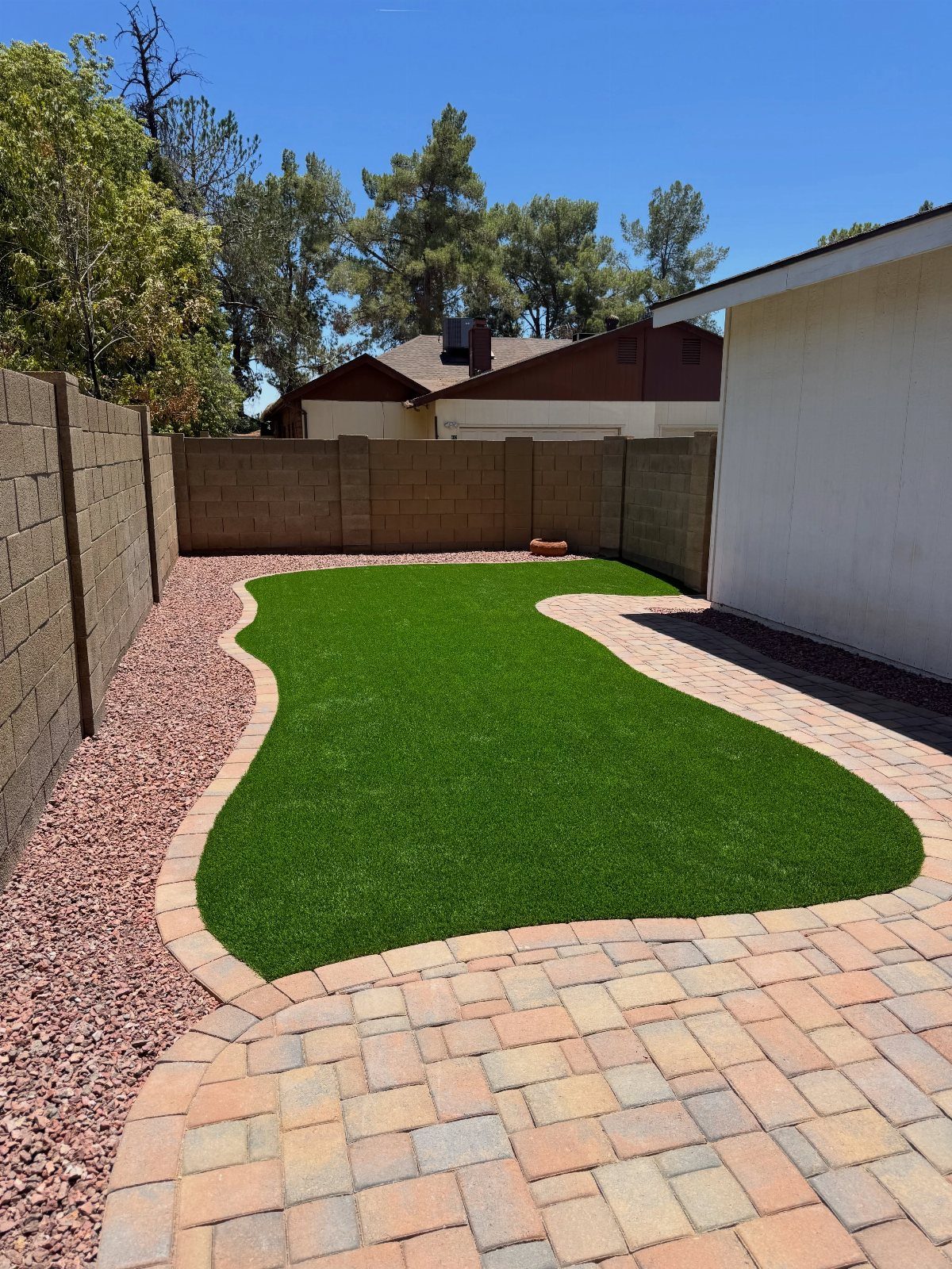 A curved stone paver walkway bordering a patch of green artificial turf in a backyard.