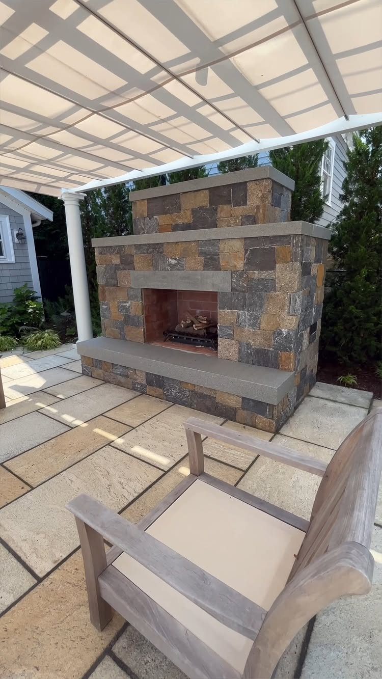 A stone outdoor fireplace built with multi-colored masonry blocks on a light stone patio.
