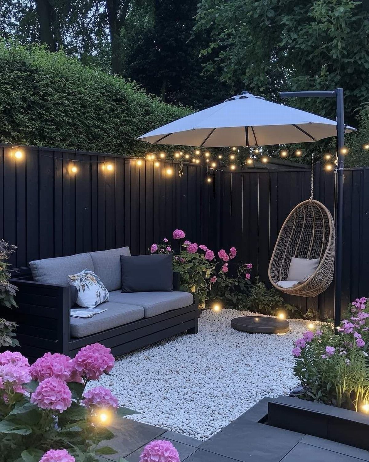 A cozy backyard patio with a grey sofa, hanging chair, and glowing string lights.