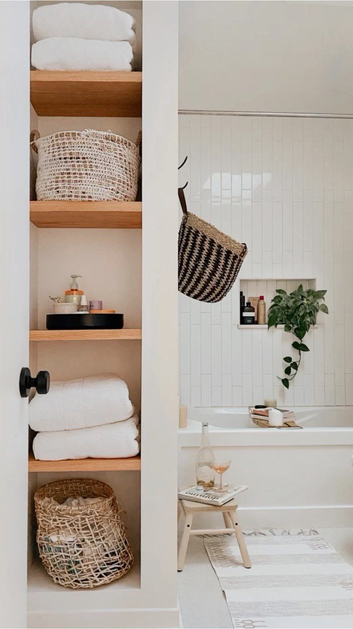 White built-in bathroom closet with wooden shelves holding folded towels and woven storage baskets.