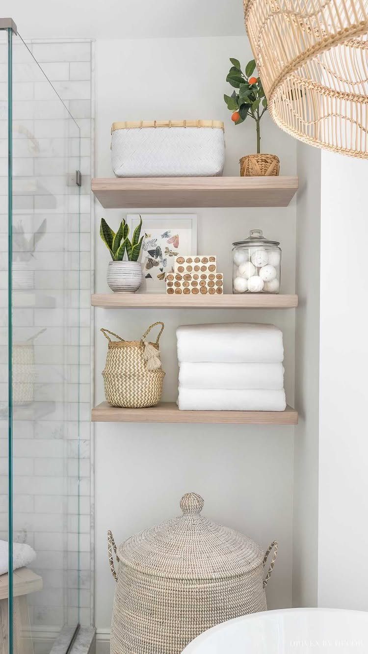 Three wooden floating shelves holding white towels, baskets, and toiletries on a white wall.