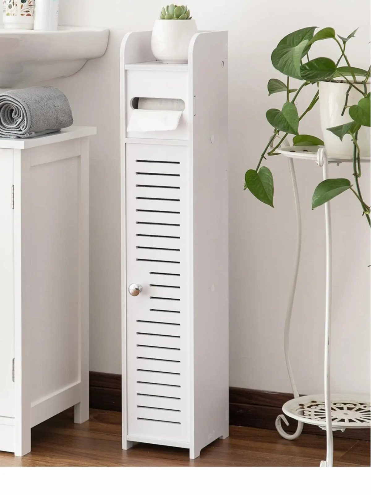 Tall slim white wooden storage cabinet with slatted door standing on a wooden floor.