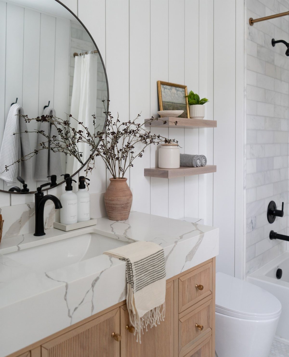 Two wooden floating shelves mounted on white shiplap wall above a marble bathroom vanity.