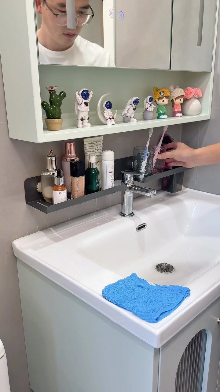 A hand reaches for toiletries on a narrow shelf mounted above a white bathroom sink.