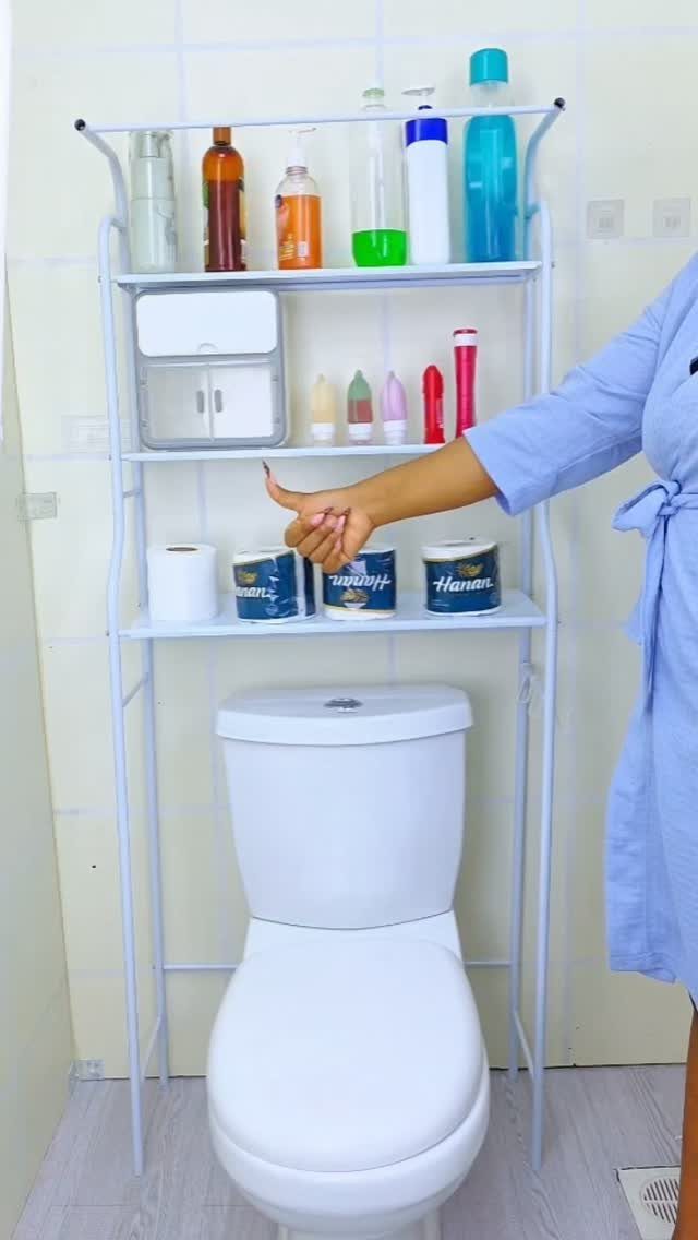 A white metal three-tier storage rack holding various bathroom supplies behind a white toilet.