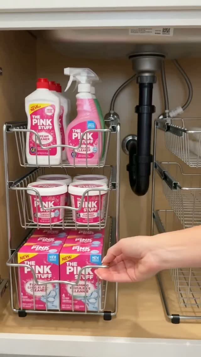 Silver wire tiered organizer holding Pink Stuff cleaning products inside a bathroom vanity cabinet under a sink.