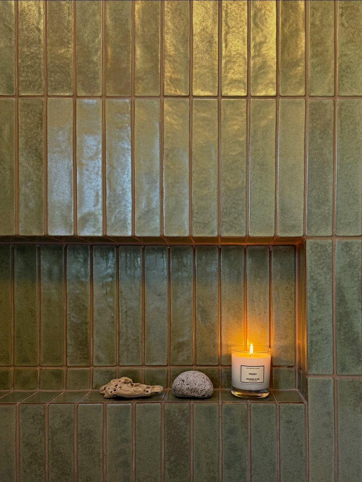 Olive green vertical subway tiles on a wall with a recessed shelf containing a candle.