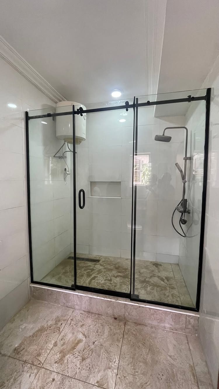 A walk-in shower featuring clear glass doors with black metal frames and white tiled walls.