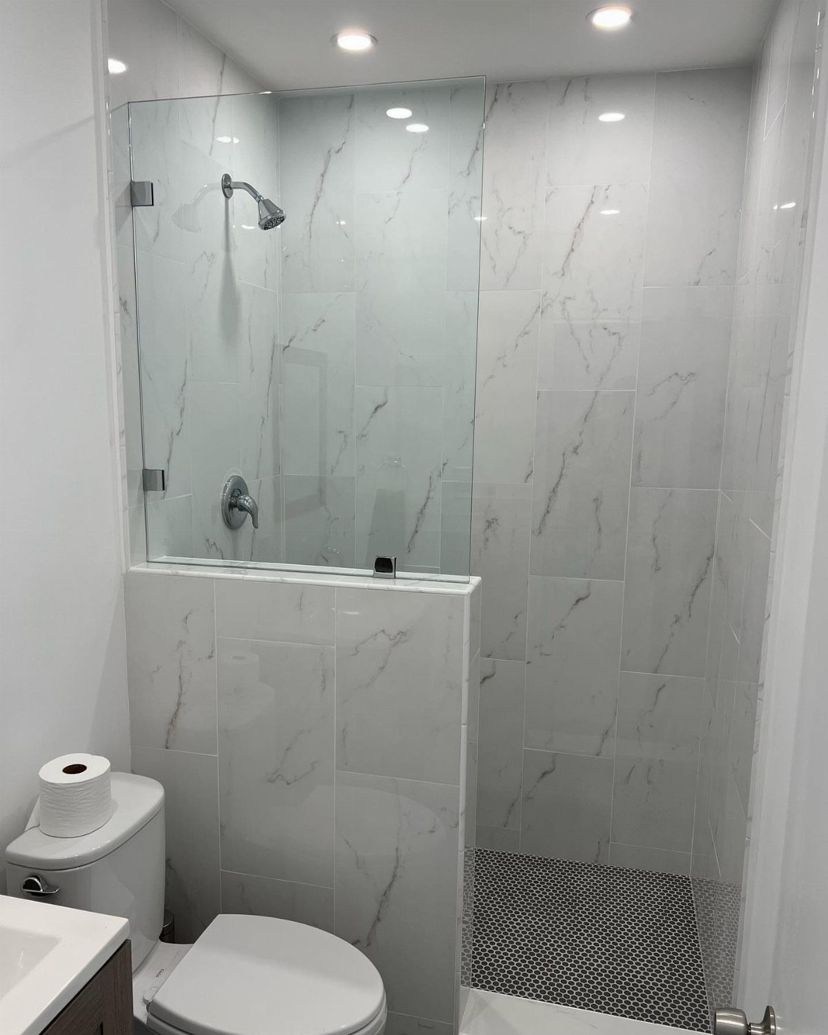 A walk-in shower with marble tiles and a clear glass door in a small bathroom.