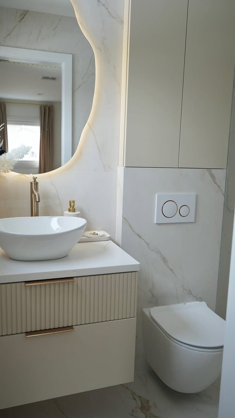 White vessel sink on a floating vanity with a backlit mirror and wall-mounted toilet.