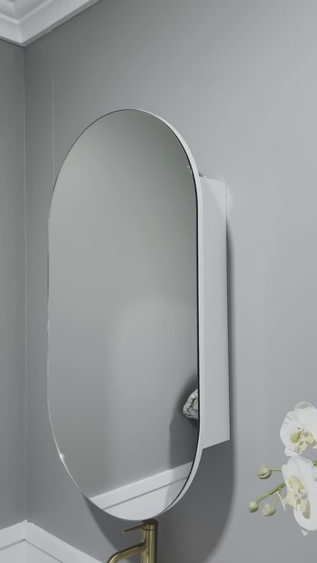 An oval white medicine cabinet mounted on a grey wall above a gold bathroom faucet.