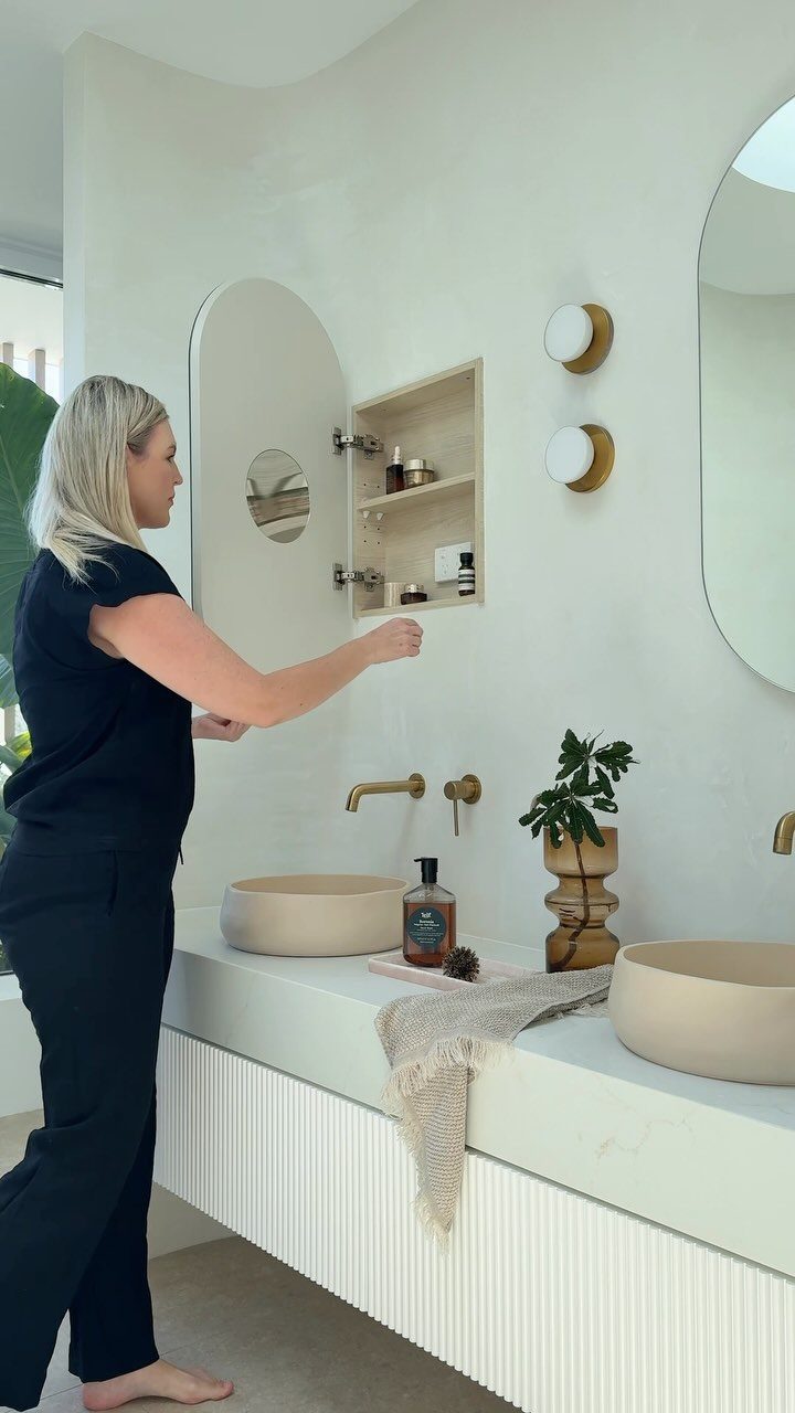 A woman reaches into an open recessed wooden medicine cabinet mounted in a white bathroom wall.