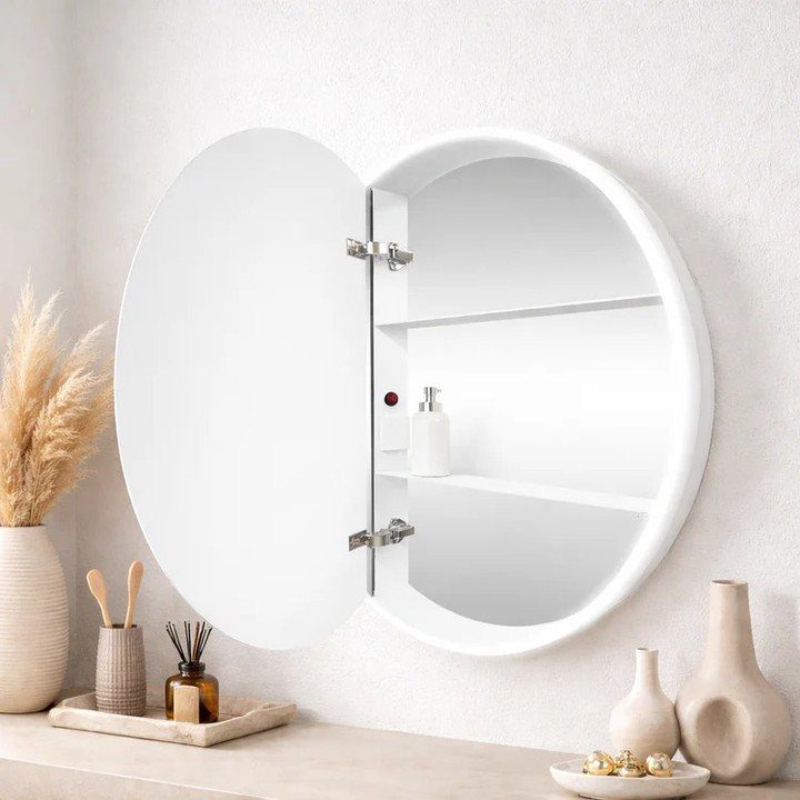 A round white medicine cabinet with an open mirror door showing interior shelves on a wall.
