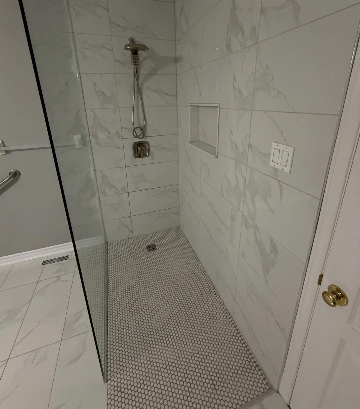 A walk-in shower featuring marble tiles and a white pebble floor with no curb.