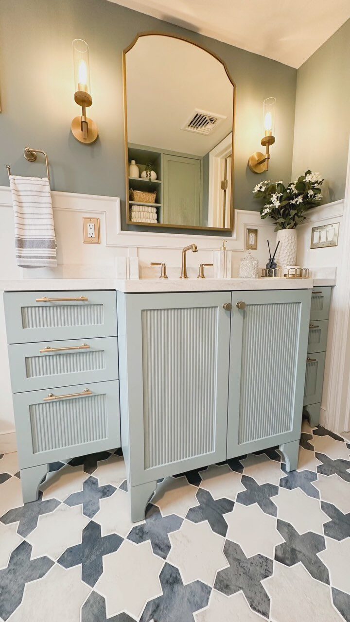 Light blue fluted bathroom vanity with gold hardware and patterned floor tiles.