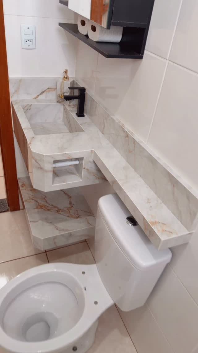 Marble countertop extending from a sink over a white toilet in a small bathroom.