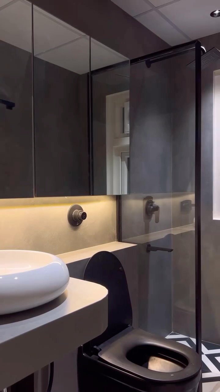Modern bathroom with a white vessel sink, black toilet, and large mirrored cabinets above the counter.
