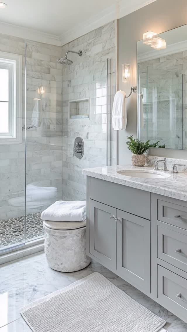 A modern bathroom with grey cabinets, marble countertops, and light grey marble wall tiles.