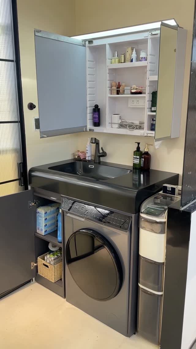 Black bathroom countertop with an open wall cabinet and integrated washing machine with side storage shelves.