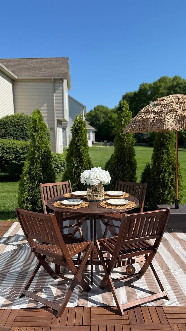 Wooden folding bistro set with four chairs and a round table on a striped rug outdoors.