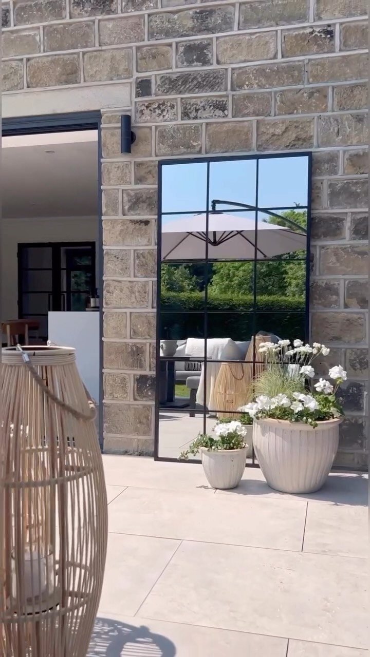 A large black-framed mirror leaning against a stone wall on a sunny outdoor patio.
