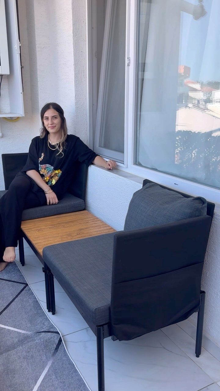 A woman sitting on grey modular outdoor patio furniture with a wooden table section.