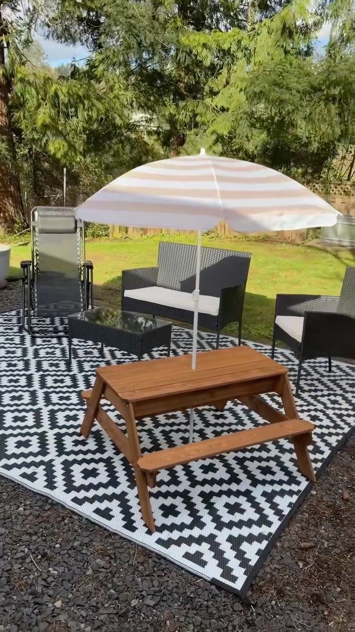 A black and white geometric patterned outdoor rug under a wooden picnic table and patio furniture.